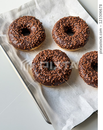 Brown chocolate donuts on metal tray and white table top view Brown chocolate donuts on metal tray and white table top view 123306678
