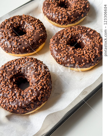 Brown chocolate donuts on metal tray and white table close up 123306684
