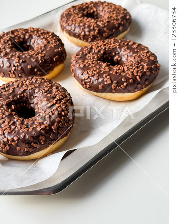 Brown chocolate donuts on metal tray and white table close up Brown chocolate donuts on metal tray and white table close up 123306734