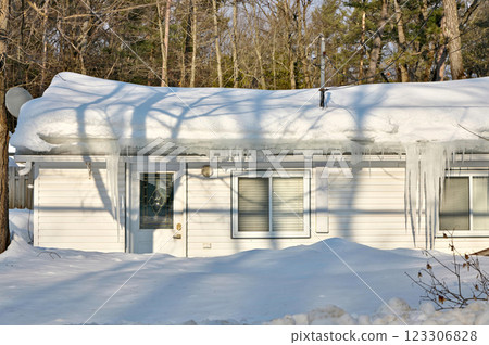Large icicles and ice dams form at the edge of the snow-covered roof above frozen eavestrough gutter 123306828
