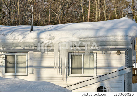 Large icicles and ice dams form at the edge of the snow-covered roof above frozen eavestrough gutter Large icicles and ice dams form at the edge of the snow-covered roof above frozen eavestrough gutter 123306829