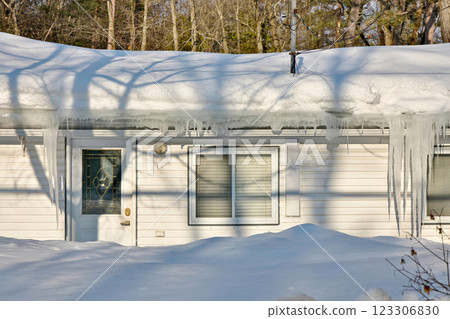Large icicles and ice dams form at the edge of the snow-covered roof above frozen eavestrough gutter 123306830