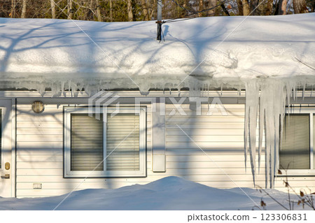 Large icicles and ice dams form at the edge of the snow-covered roof above frozen eavestrough gutter 123306831