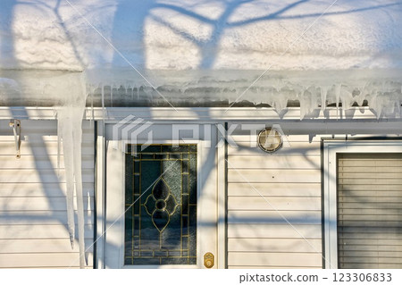 Large icicles and ice dams form at the edge of the snow-covered roof above frozen eavestrough gutter 123306833