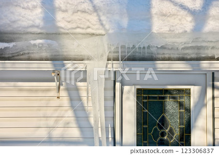 Large icicles and ice dams form at the edge of the snow-covered roof above frozen eavestrough gutter 123306837