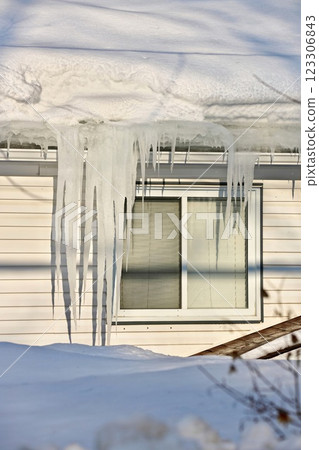 Large icicles and ice dams form at the edge of the snow-covered roof above frozen eavestrough gutter 123306843