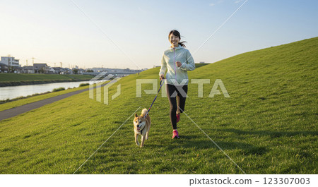 A woman jogging with her dog on the riverbank 123307003