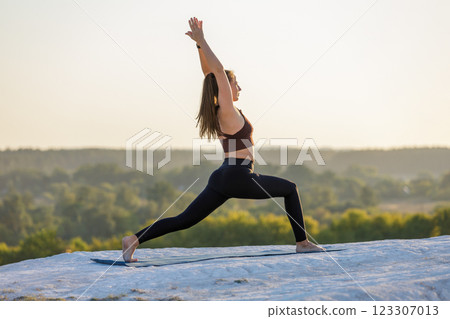 Young woman performing yoga high lunge pose at sunset on a scenic overlook Young woman performing yoga high lunge pose at sunset on a scenic overlook 123307013