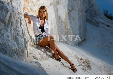Woman in white shirt and denim shorts poses on white stone in natural setting 123307061