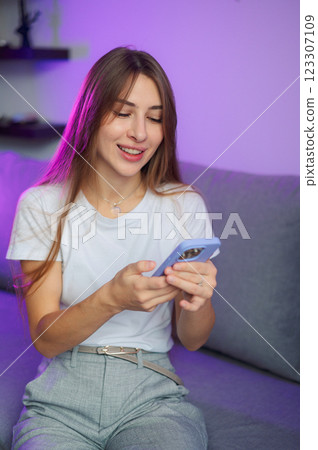 Cheerful smiling young woman is having a pleasant phone conversation, enjoying a moment of connection and laughter in the comfort of her home purple light Cheerful smiling young woman is having a pleasant phone conversation, enjoying a moment of connection and laughter in the comfort of her home purple light 123307109