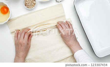 Baking Crinkle Cake., hands folding phyllo dough with egg, butter, nuts, milk 123307434