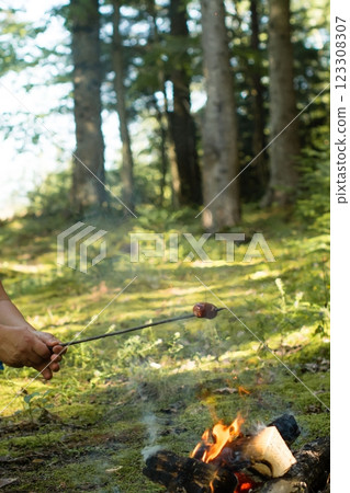 Roasting a sausage over a campfire in a forest setting. 123308307