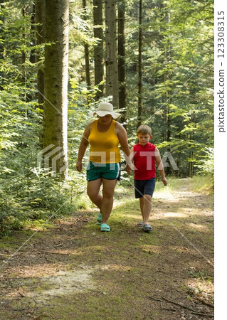A woman and child stroll along a sun-dappled forest path, enjoying a leisurely walk among the trees. 123308315