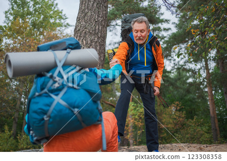 Hiking adventure. Man helping hand woman on hiking in forest. Senior couple enjoying outdoor recreation hiking. Happy old people backpackers hikers enjoy walking hike trekking tourism active vacation 123308358