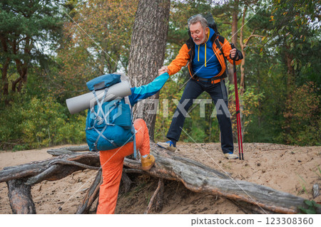 Hiking adventure. Man helping hand woman on hiking in forest. Senior couple enjoying outdoor recreation hiking. Happy old people backpackers hikers enjoy walking hike trekking tourism active vacation 123308360