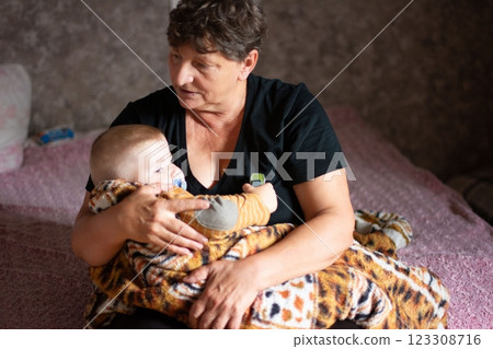A woman sits indoors, cradling a baby wrapped in a tiger-striped blanket, both figures exhibiting tranquility in a familial moment. A woman sits indoors, cradling a baby wrapped in a tiger-striped blanket, both figures exhibiting tranquility in a familial moment. 123308716