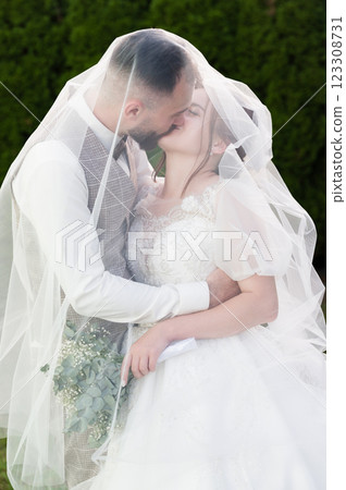 Bride and groom share a tender kiss, veiled in romance under a sheer wedding veil. Bride and groom share a tender kiss, veiled in romance under a sheer wedding veil. 123308731