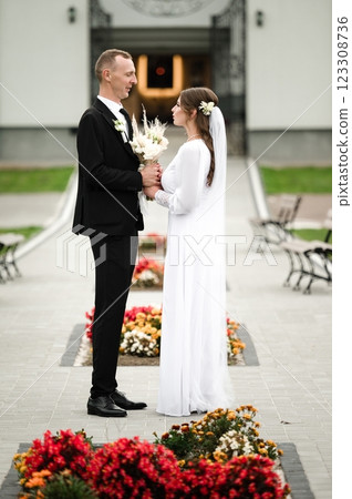 A bride and groom share a tender moment, holding hands and exchanging loving glances. They stand amidst vibrant flowers, creating a romantic atmosphere. A bride and groom share a tender moment, holding hands and exchanging loving glances. They stand amidst vibrant flowers, creating a romantic atmosphere. 123308736