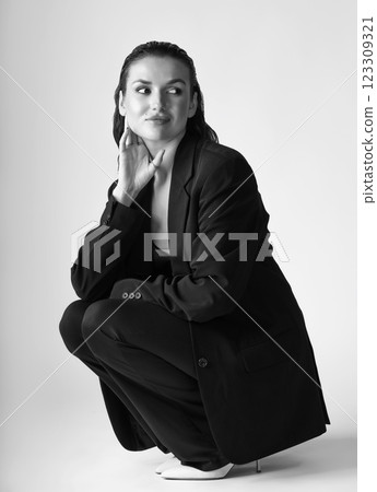 Studio portrait of beautiful woman with black suit and wet hair squatting on floor Studio portrait of beautiful woman with black suit and wet hair squatting on floor 123309321