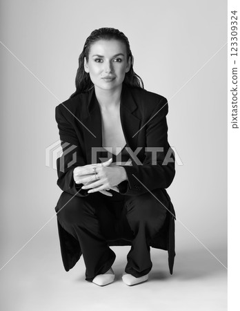 Studio portrait of beautiful woman with black suit and wet hair squatting on floor Studio portrait of beautiful woman with black suit and wet hair squatting on floor 123309324
