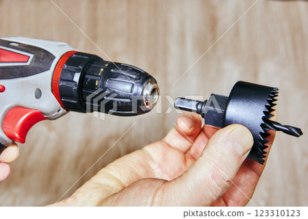 Cordless drill aligning with a door lock hole saw attachment and drill bit, ready for precise woodworking. Cordless drill aligning with a door lock hole saw attachment and drill bit, ready for precise woodworking. 123310123