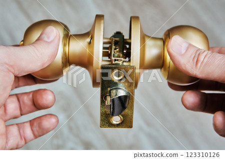 Door knob held by hands, showcases latch mechanism and brass finish, revealing workings of typical door handle against neutral background. Door knob held by hands, showcases latch mechanism and brass finish, revealing workings of typical door handle against neutral background. 123310126