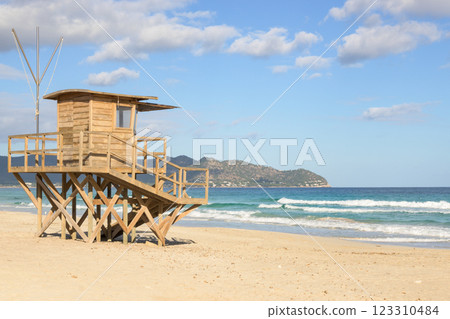 A wooden lifeguard tower on a sandy beach with ocean waves and mountains in view, mallorca balearic islands, spain A wooden lifeguard tower on a sandy beach with ocean waves and mountains in view, mallorca balearic islands, spain 123310484