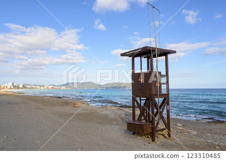 A rustic lifeguard tower stands on a beach overlooking the ocean and distant mountains, mallorca balearic islands, spain A rustic lifeguard tower stands on a beach overlooking the ocean and distant mountains, mallorca balearic islands, spain 123310485