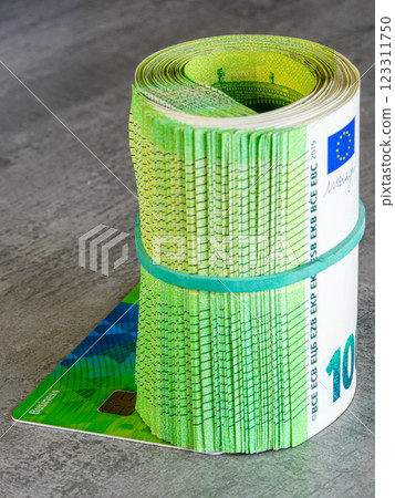 A thick roll of green 100 euro banknotes tied with a rubber band placed on a business payment card A thick roll of green 100 euro banknotes tied with a rubber band placed on a business payment card 123311750