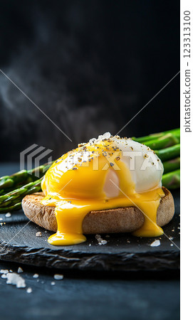 indulgent eggs benedict with poached egg and golden hollandaise sauce on rustic stone plate, fresh asparagus spears, dark slate background, gourmet breakfast, moody food photography 123313100
