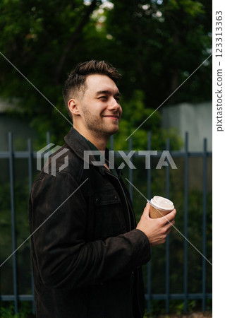 Vertical side view of happy relaxed young man in casual attire, holding coffee cup, enjoying peaceful break outdoors, radiating calm and contentment in urban setting. Concept of urban lifestyle. Vertical side view of happy relaxed young man in casual attire, holding coffee cup, enjoying peaceful break outdoors, radiating calm and contentment in urban setting. Concept of urban lifestyle. 123313363