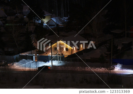 Winter night charm revealed as soft lights glimmer through the snowy landscape near quiet suburban homes 123313369
