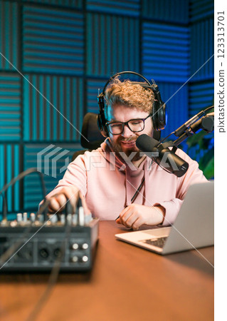 Cheerful young man recording podcast in studio. Confident man with headphones and microphone recording a podcast. Happy guy talking on web radio. Cheerful young man recording podcast in studio. Confident man with headphones and microphone recording a podcast. Happy guy talking on web radio. 123313701