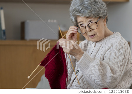 A woman in her 80s pushes her glasses aside to look at her knitting stitches 123315688
