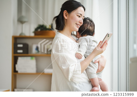A woman looking at her smartphone while holding a baby A woman looking at her smartphone while holding a baby 123315999