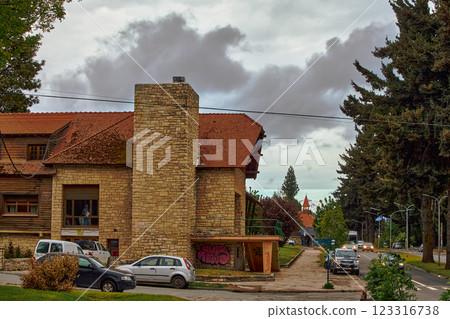 Building with tile roof on shore in thicket of trees, against dark clouds 123316738