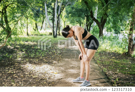 Sporty young woman tired from running. A sporty girl taking a break after running. Concept of sporty girl tired and taking a break after running 123317310