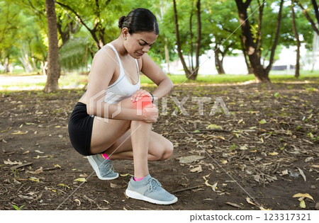 Athlete woman with knee muscle pain. Athlete girl on the ground with knee pain outdoors. Runner woman with knee pain outdoors. Athlete knee pain and fractures concept Athlete woman with knee muscle pain. Athlete girl on the ground with knee pain outdoors. Runner woman with knee pain outdoors. Athlete knee pain and fractures concept 123317321