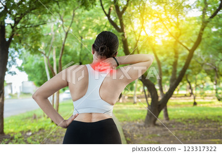 Running woman with shoulder muscle pain in a park. Shoulder pain concept of a runner athlete. Athlete girl in pain rubbing her shoulder outdoors. Back view of sporty woman with shoulder pain 123317322