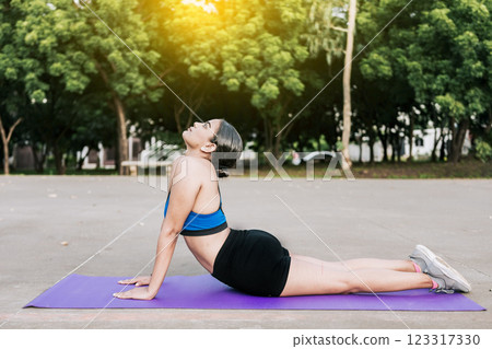Sporty woman stretching her body doing cobra pose in a park. Athlete woman doing cobra pose in a park. Athlete woman doing yoga Bhujangasana in a park Sporty woman stretching her body doing cobra pose in a park. Athlete woman doing cobra pose in a park. Athlete woman doing yoga Bhujangasana in a park 123317330