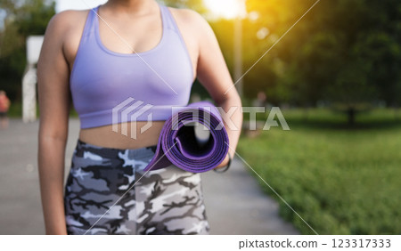 Unrecognizable woman holding a mat in the park. Athlete woman's hands carrying the mat after exercising. Fitness woman concept carrying yoga mat with copy space 123317333