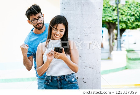 Jealous man spying on his girlfriend texting on the cell phone. Suspicious man spying on his girlfriend with his cell phone, Jealous boyfriend spying on his girlfriend's cell phone in the park Jealous man spying on his girlfriend texting on the cell phone. Suspicious man spying on his girlfriend with his cell phone, Jealous boyfriend spying on his girlfriend's cell phone in the park 123317359
