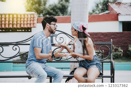 Man arguing with his girlfriend sitting in a park. Young couple arguing sitting on a park bench, Concept of aggressive couples in the park. Upset couple arguing on a park bench Man arguing with his girlfriend sitting in a park. Young couple arguing sitting on a park bench, Concept of aggressive couples in the park. Upset couple arguing on a park bench 123317362
