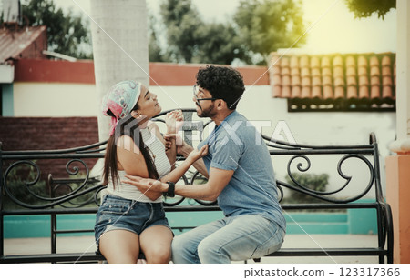Man arguing with girlfriend sitting in a park. Young couple arguing sitting on a park bench, Concept of aggressive couples in the park. Upset couple arguing on a park bench Man arguing with girlfriend sitting in a park. Young couple arguing sitting on a park bench, Concept of aggressive couples in the park. Upset couple arguing on a park bench 123317366
