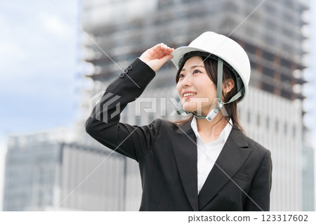 A young woman in a suit and helmet standing at a construction site, construction manager, site supervisor, female civil engineer (Dobojo) 123317602