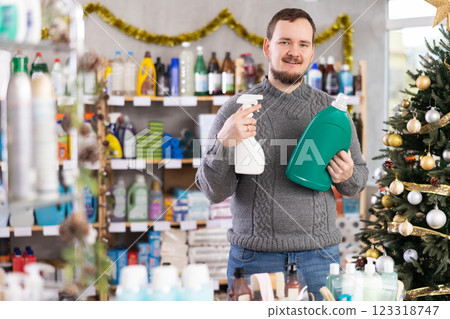 Positive young man choosing liquid detergent and spray at household goods in store decorated for New Year holiday 123318747