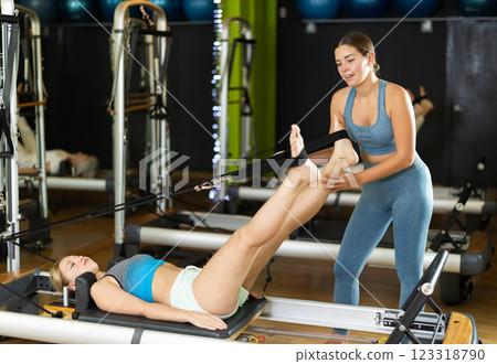 Female trainer helps to do leg exercises on the reformer 123318790