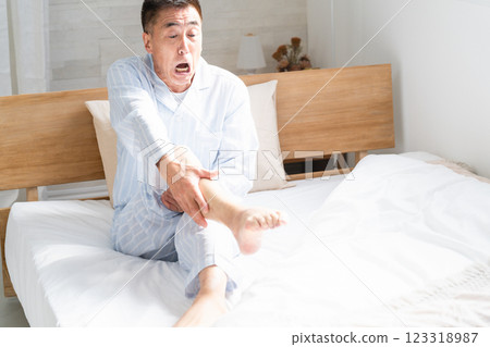 A man waking up in bed with cramps in his legs 123318987