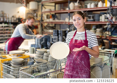 Enthusiastic female ceramicist demonstrating handcrafted plates in studio 123319225