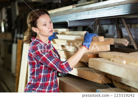 Woman employee of carpentry workshop takes out necessary board from stack of materials 123319242
